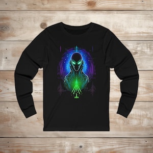 May include: Black long-sleeve shirt featuring a neon green and blue alien graphic. The design includes a detailed illustration of an extraterrestrial figure with glowing eyes and a geometric pattern.
