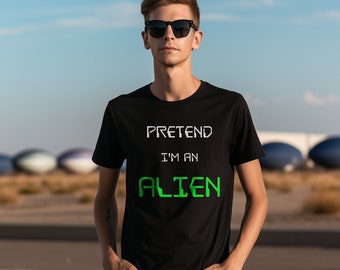 May include: A black t-shirt with the text "PRETEND I'M AN ALIEN" in white and green. The person in the image is wearing black sunglasses and has their hands in their pockets. The background is a blue sky.