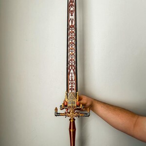 May include: A decorative sword with a gold and red handle and a silver blade. The blade is decorated with intricate patterns.