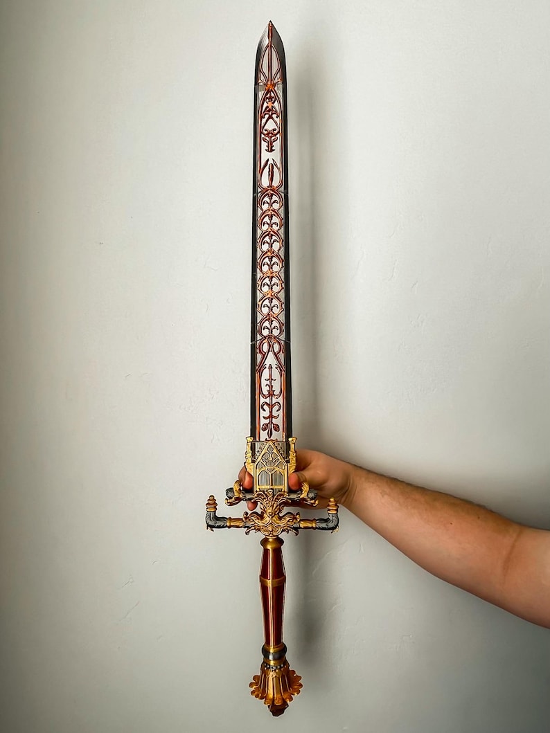 May include: A decorative sword with a gold and red handle and a silver blade. The blade is decorated with intricate patterns.
