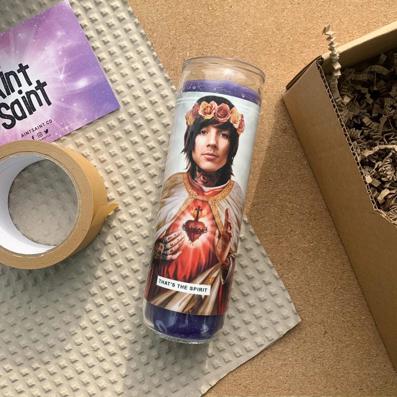Pode incluir: Uma vela de vidro roxo com uma imagem impressa de um homem com uma coroa de flores na cabe&ccedil;a. O homem est&aacute; vestindo uma t&uacute;nica branca com um cora&ccedil;&atilde;o vermelho no peito. O texto "That's the Spirit" est&aacute; impresso abaixo da imagem.
