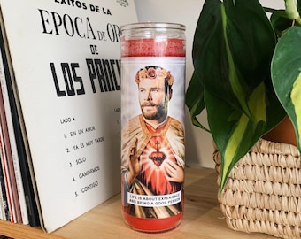 May include: Red glass candle with a printed image of a man with a beard and a flower crown. The text on the candle reads "Life is about experience and being a good person."
