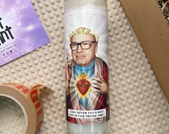 May include: A white candle with a colorful image of a man wearing a crown of flowers and a blue and red robe. The text on the candle reads "Can I offer you a nice egg in this trying time?"