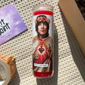 Pode incluir: Vela vermelha de vidro com uma imagem impressa de uma pessoa com uma coroa de flores, um cora&ccedil;&atilde;o vermelho e o texto "THAT'S THE SPIRIT".