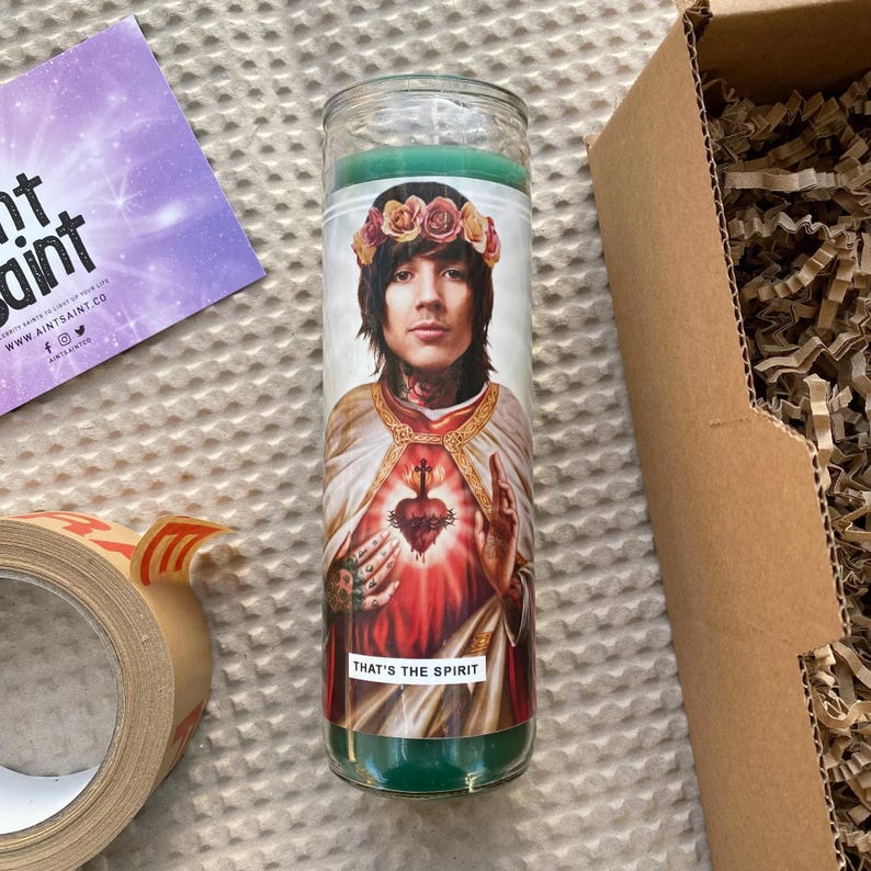 Pode incluir: Uma vela de vidro verde com uma imagem impressa de um homem com uma coroa de flores na cabe&ccedil;a. O homem est&aacute; vestindo uma t&uacute;nica branca e segurando um cora&ccedil;&atilde;o em suas m&atilde;os. O texto "That's the spirit" est&aacute; impresso na parte inferior da vela.