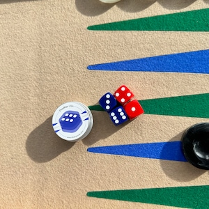 May include: A close-up of a backgammon board with blue and green triangles, four red dice, one blue die, and a silver container with a blue die logo and the text "DiceMan USA" and "www.dice-man.com".