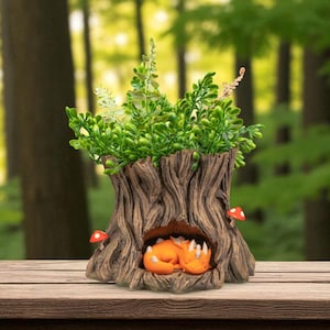 May include: A whimsical tree stump planter with a sleeping fox figurine inside. The planter is filled with green foliage and accented with red mushroom details. The planter is made of a brown material.