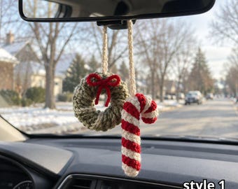 Pode incluir: Um ornamento de crochê para espelho retrovisor de carro com uma pequena guirlanda verde-oliva com um laço vermelho e uma bengala doce com listras vermelhas e brancas, pendurados por alças de fio creme. O texto "style 1" é visível no canto.