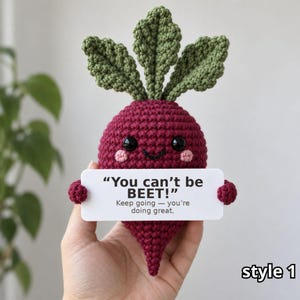May include: A dark red crocheted beet plush toy with green leaves, black eyes, and pink cheeks. It holds a white rectangular sign that reads: "You can't be BEET!" followed by the text "Keep going — you're doing great." in black lettering.