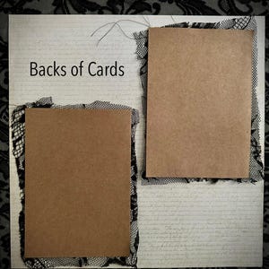 May include: A craft paper card with the text "Backs of Cards" is displayed on a textured background. The card is framed with black lace. Two additional craft paper cards are also framed with black lace.