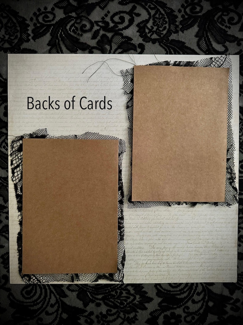 May include: A craft paper card with the text "Backs of Cards" is displayed on a textured background. The card is framed with black lace. Two additional craft paper cards are also framed with black lace.