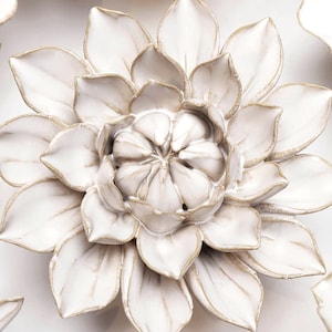 May include: A collection of white ceramic flower wall decor. The flowers have a raised, textured design and are accented with gold trim. The flowers are arranged in a circular pattern on a white background.