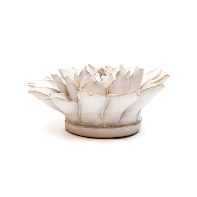 May include: A white ceramic lotus flower sculpture with gold trim. The flower has multiple petals and sits on a round base. The sculpture is a decorative item.