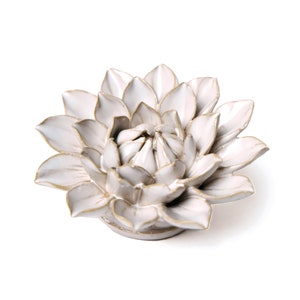 May include: A white ceramic flower sculpture with a detailed petal design and gold-colored accents. The flower is centered on a white background, showcasing its intricate form. This decorative piece is ideal for home decor.