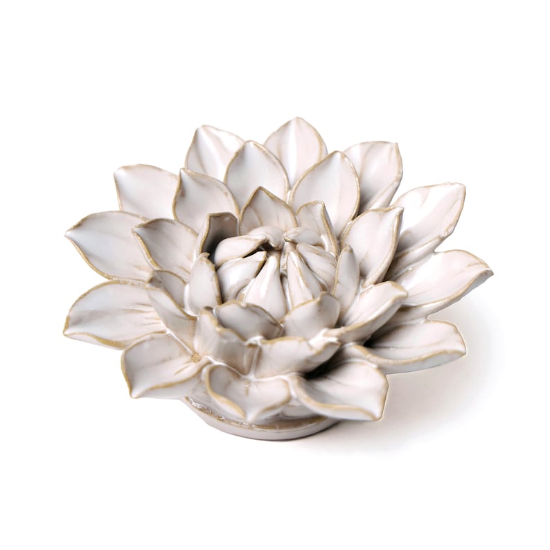 May include: A white ceramic flower sculpture with a detailed petal design and gold-colored accents. The flower is centered on a white background, showcasing its intricate form. This decorative piece is ideal for home decor.