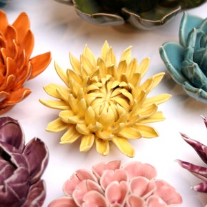 May include: A collection of ceramic flower wall decor in various colors, including yellow, orange, pink, purple, and blue. The flowers are all in a realistic style and have a 3D effect.
