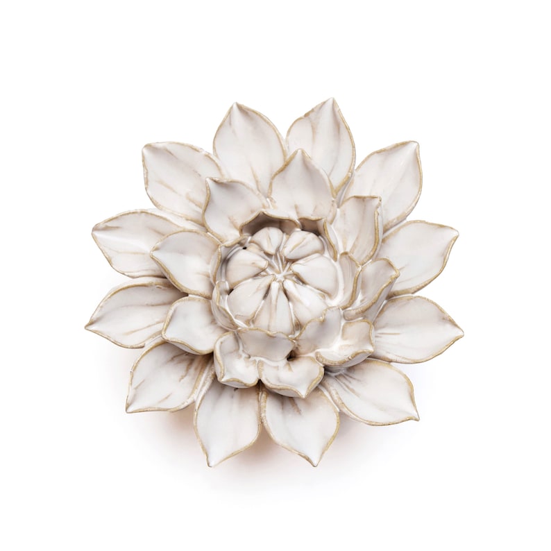 May include: A white ceramic flower sculpture with gold-colored edges. The flower has multiple layers of petals, creating a detailed and textured appearance. The sculpture is a decorative item, likely for wall mounting or display.