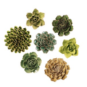 May include: A collection of ceramic flower sculptures in various shades of green and tan. The floral designs include a variety of shapes and textures, with some featuring layered petals and others with a more compact, rounded form. The sculptures are arranged on a white background.