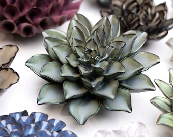 May include: A collection of ceramic flower wall decor in various colors and styles. The flowers are made of a textured ceramic and have a realistic appearance. The flowers are arranged in a cluster on a white background.