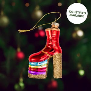 May include: A red high-heeled boot Christmas ornament with a gold glitter platform and heel. The ornament has a gold hanging string and the text "100+ STYLES AVAILABLE" in a white circle.