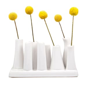 May include: White ceramic vase with multiple openings for flowers. The vase has a modern design and is filled with yellow billy balls.