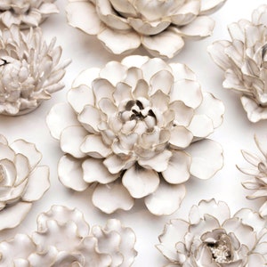 May include: A set of nine white ceramic wall flowers with a subtle gold trim. The flowers are arranged in a variety of sizes and shapes, creating a beautiful and elegant display.