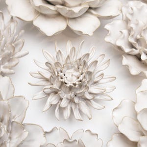 May include: A set of white ceramic flowers with a textured finish. The flowers are arranged in a circular pattern on a white background.