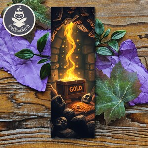Puede incluir: Un marcapáginas rectangular con una ilustración de fantasía de un cofre de madera con la etiqueta GOLD, rebosante de luz amarilla brillante y monedas. La escena muestra una cueva de piedra oscura con calaveras y rocas en tonos marrones, grises y amarillos.