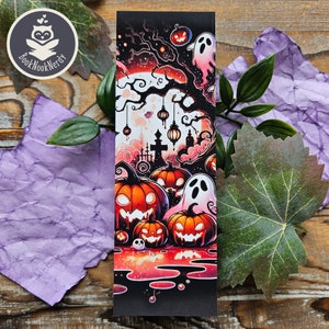 May include: A rectangular bookmark featuring a vibrant Halloween illustration with orange jack-o'-lanterns, white ghosts, and a dark tree silhouette against a large moon. The design includes hanging lanterns, a graveyard scene, and red accents.