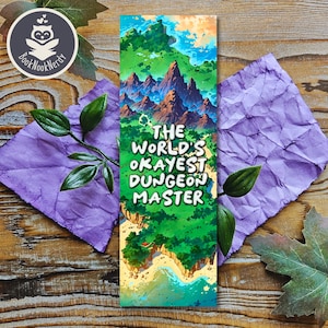 Könnte beinhalten: Ein grünes und blaues Lesezeichen mit einer Illustration einer Fantasieinsel und dem Text "The World's Okayest Dungeon Master".