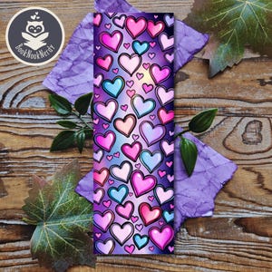 May include: A purple bookmark featuring a pattern of pink, blue and white hearts. The hearts are outlined in black and have a gradient effect.