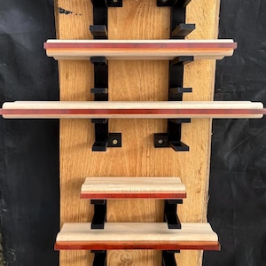 May include: A wooden wall shelf unit with five shelves of varying sizes. The shelves have a light wood base with a red and orange accent. The shelves are supported by black metal brackets. The unit is mounted on a large, light-colored wooden plank.