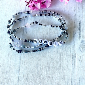 May include: A multi-layered beaded necklace with black and silver beads. The necklace has white letter beads that spell out the name "WONBIN".