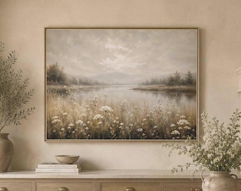 Pode incluir: Uma pintura de paisagem retangular numa moldura dourada fina representando um lago calmo rodeado por campos de flores silvestres de tons suaves e colinas distantes, exibida numa parede de tons neutros sobre uma bancada de cozinha.
