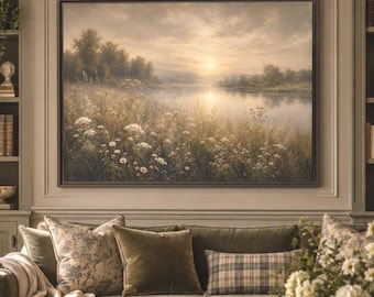 May include: A large rectangular landscape painting depicting a sunset over a calm river and wildflower field, framed in dark wood. The artwork hangs above a sage green sofa adorned with patterned and solid velvet throw pillows and a cream throw.