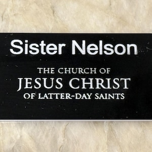 Könnte beinhalten: Schwarzer Namensschild mit weißem Text, der "Schwester Nelson, Die Kirche Jesu Christi der Heiligen der Letzten Tage" lautet.