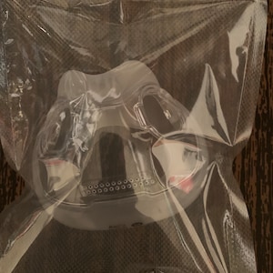 May include: A white plastic face mask with a clear plastic nose piece and a black elastic strap. The mask has a series of small holes around the edge.
