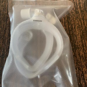 May include: A clear plastic bag with a white label that says "STANDARD" inside. The bag contains a white, coiled cable.