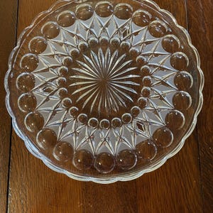 May include: A clear glass cake stand with a decorative pattern of raised circles and diamond shapes.