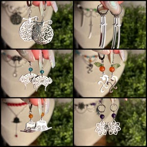 May include: A collection of six pairs of silver-toned metal earrings featuring various designs including swirling patterns, miniature swords, hat shapes, and floral motifs, accented with small colourful beads and suspended from circular hoop findings.