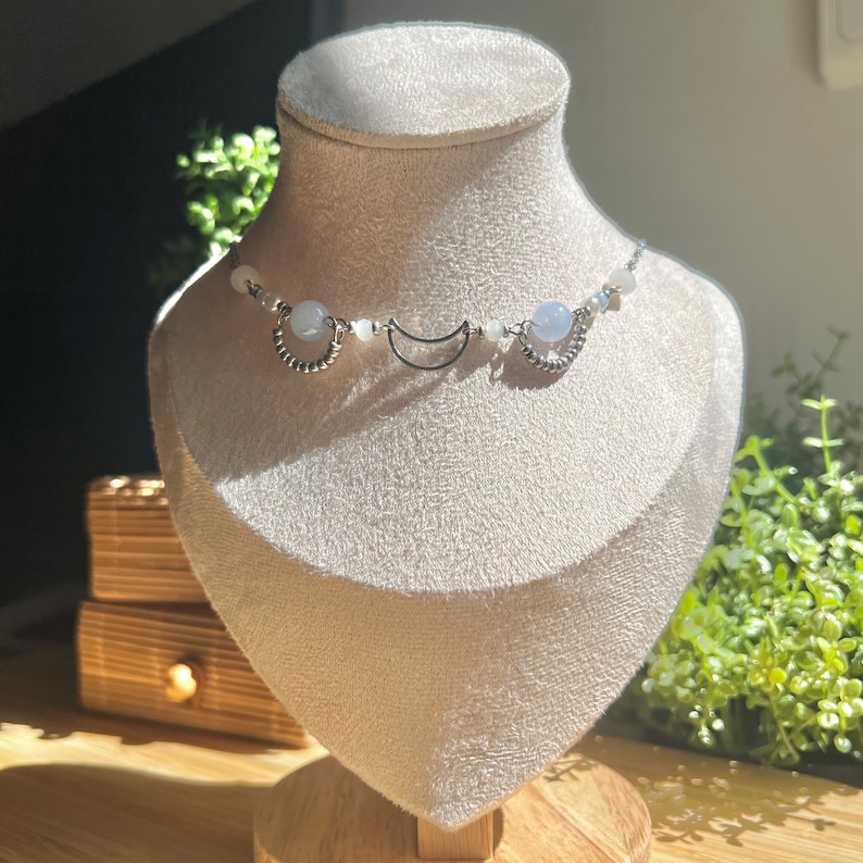 Op de afbeelding: Een zilveren choker ketting met blauwe en witte kralen en halve maan bedels.