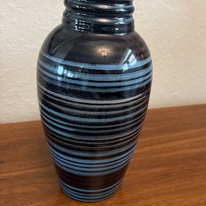 Puede incluir: Un jarrón de cerámica alto, rayado en negro y azul, con un acabado brillante.