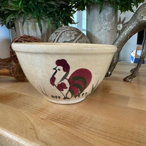 Puede incluir: Un tazón de mezcla de cerámica vintage con un diseño de gallo. El tazón es de color crema con un gallo rojo, verde y blanco pintado en el lateral.