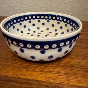 Può includere: Una ciotola in ceramica bianca con un motivo a pois blu e bianchi. La ciotola ha un bordo blu con un accento bianco e oro.
