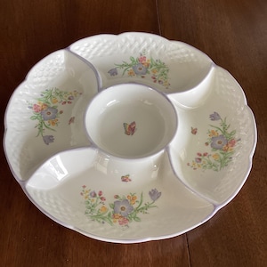 Puede incluir: Un plato de servir de cerámica blanca con cinco secciones, con un diseño floral con flores moradas, amarillas y rosas. La sección central es un tazón más pequeño con un diseño de mariposa.