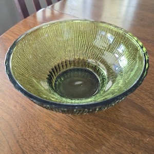 May include: A green glass bowl with a textured, ribbed design. The bowl is empty and sitting on a wooden surface.