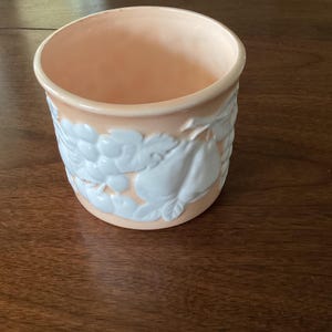 Pode incluir: Um porta-talheres de cerâmica cor de pêssego com um design em relevo branco de frutas, incluindo peras e uvas.