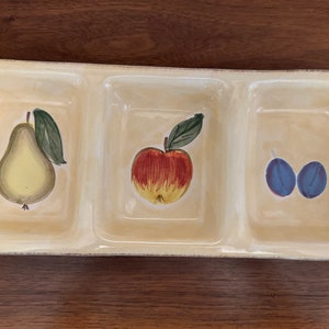 May include: A rectangular, divided serving dish with a light yellow background. Each section features a hand-painted fruit: a pear, an apple, and two plums. Green leaves and blue berries accent the design.