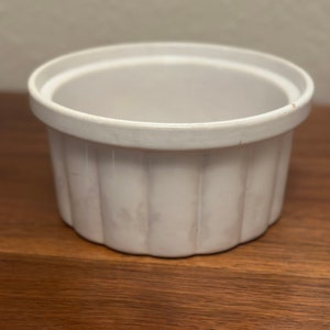 Puede incluir: Ramequín de cerámica blanca con un diseño acanalado. El ramequín está vacío y se encuentra sobre una superficie de madera.