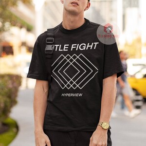 Op de afbeelding: Zwart T-shirt met een wit geometrisch ontwerp en de tekst "TITLE FIGHT" en "HYPERVIEW".